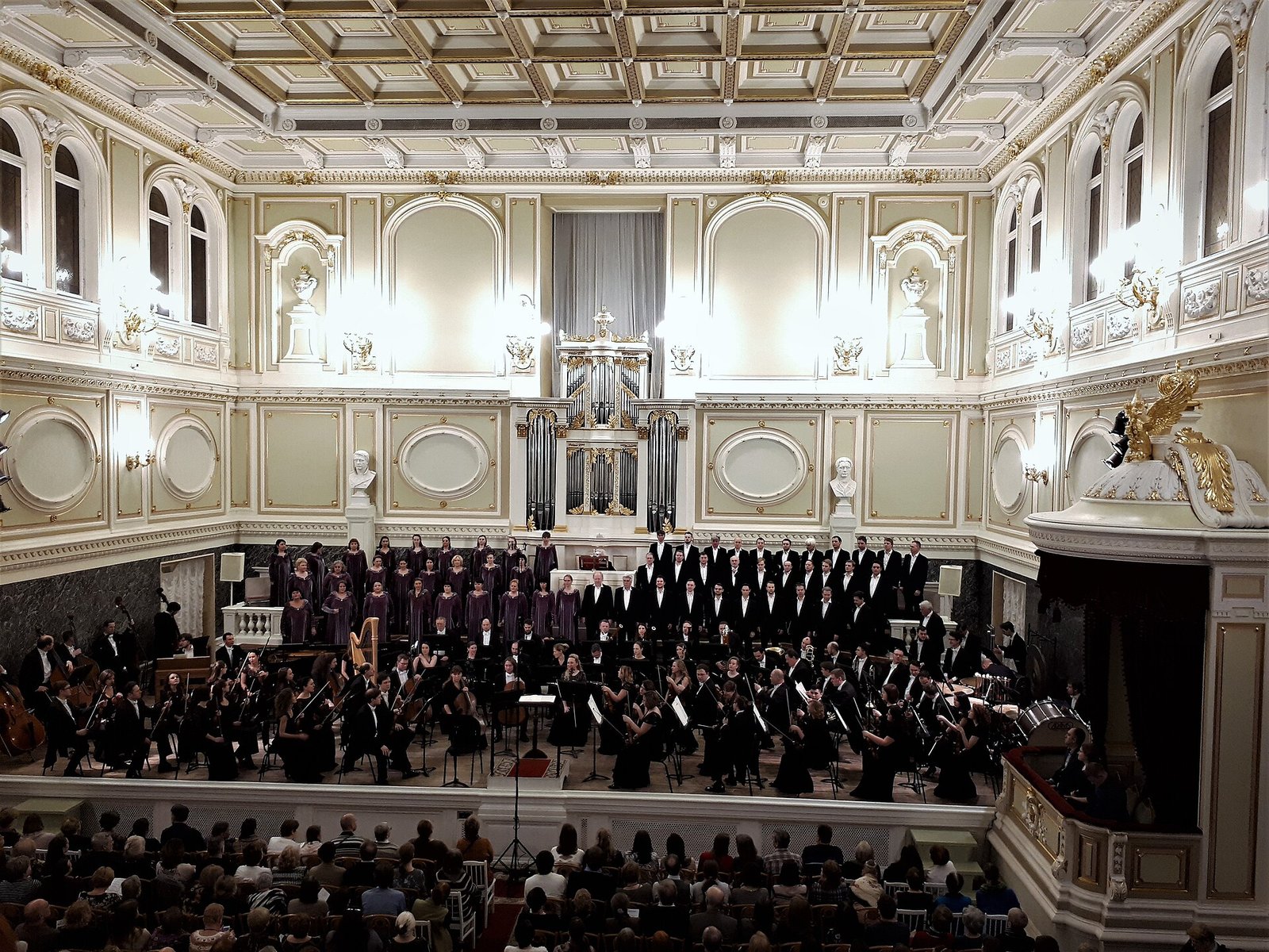 Choir and orchestra on the stage of the Capella concert hall, with the organ behind them